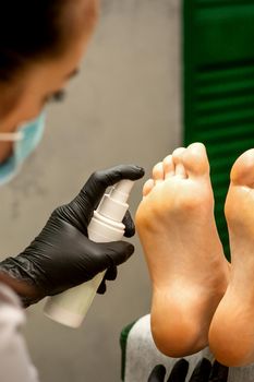 A woman getting a pedicure and pedicurist moisturizing female feet with lotion spraying in a beauty salon