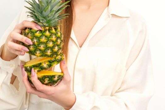 Beautiful young Caucasian woman holding pineapple and smiling, wearing a white shirt over white background