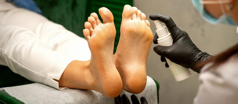 A woman getting a pedicure and pedicurist moisturizing female feet with lotion spraying in a beauty salon