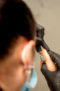 Podiatrist wearing black protective gloves cleaning the skin of foot from callus and corn with the professional electric tool