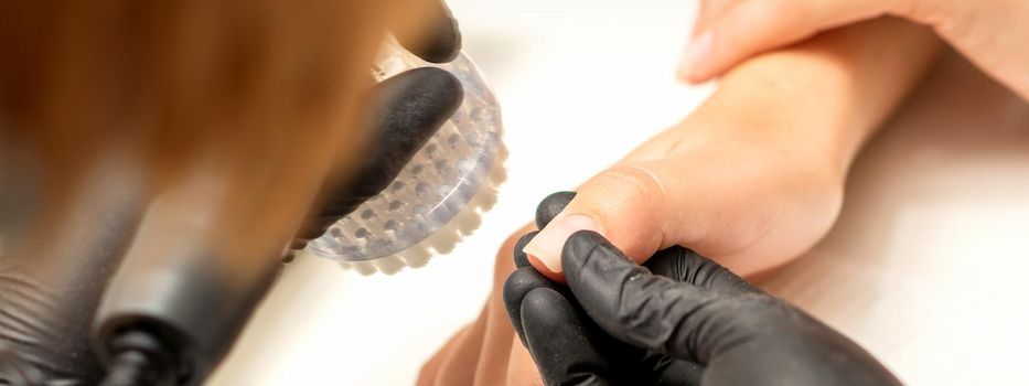 Hands of the manicure master removing dust from nails with a brush cleaning nails in a nail salon