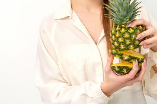 Beautiful young Caucasian woman holding pineapple and smiling, wearing a white shirt over white background