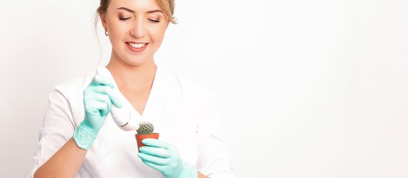 A smiling female beautician holds little green cactus with the razor in her hands. Hair removal concept