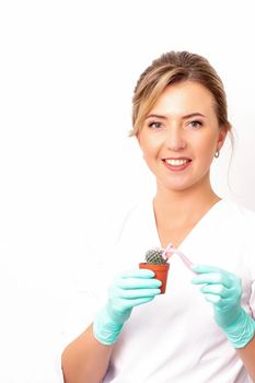 A smiling female beautician holds little green cactus with the razor in her hands. Hair removal concept