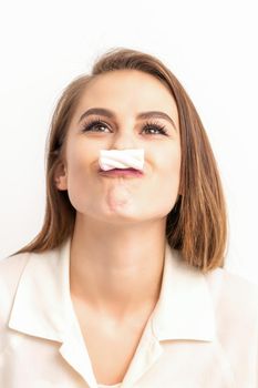 Funny young woman with marshmallow on her lips looking up and standing on white background with copy space