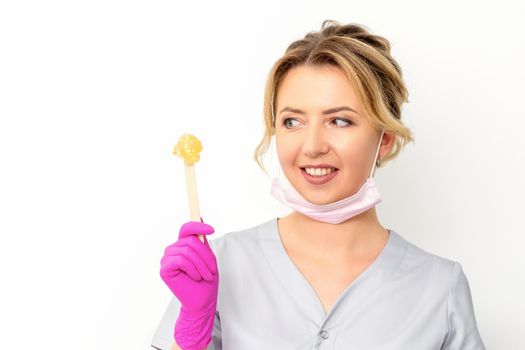 The master of sugar hair removal holds liquid yellow sugar paste, wax for depilation on a wooden stick on a white background