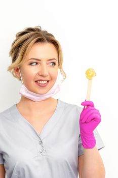 The master of sugar hair removal holds liquid yellow sugar paste, wax for depilation on a wooden stick on a white background