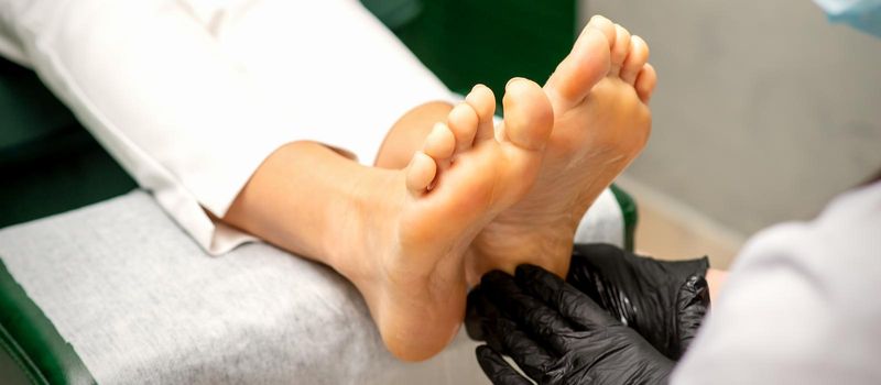 Pedicurist moisturizing female feet with lotion wearing black protective gloves in a beauty salon