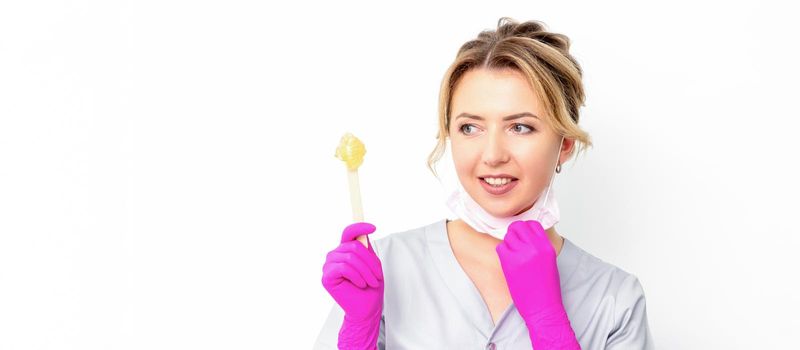 The master of sugar hair removal holds liquid yellow sugar paste, wax for depilation on a wooden stick on a white background