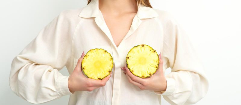 Young Caucasian smiling woman holding slices pineapple over white background, breast health concept