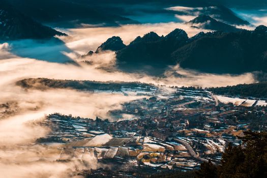 Beautiful view of a village between the mountains on a winter morning, cold weather makes the fog cover the valley and part of the village like a sea of fog.