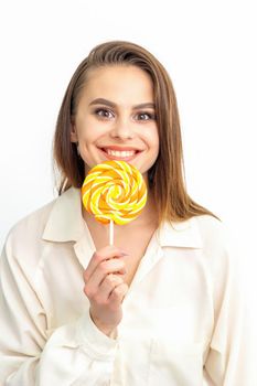 Beautiful young caucasian woman wearing a white shirt licking a lollipop on a white background