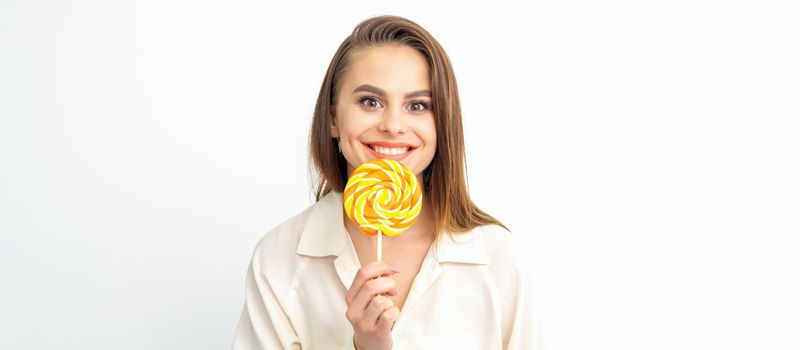 Beautiful young caucasian woman wearing a white shirt licking a lollipop on a white background