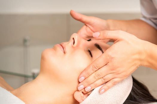 Young caucasian woman with closed eyes getting a facial massage in a beauty clinic