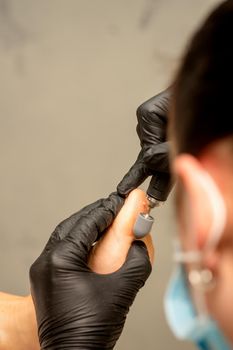 Podiatrist wearing black protective gloves cleaning the skin of foot from callus and corn with the professional electric tool