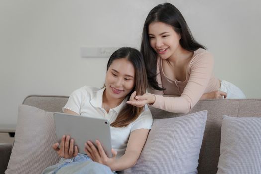 Two asian women having nice lively conversation in living room on sofa in cozy interior.