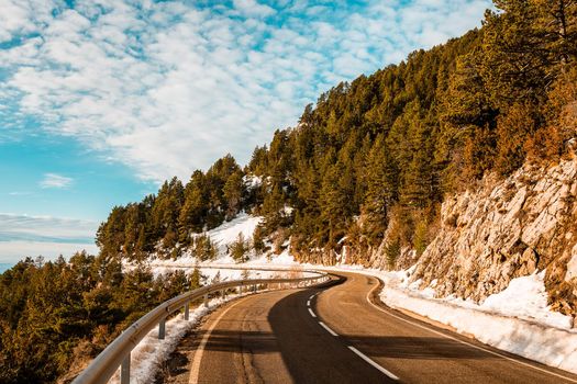 winding road in the mountains with snow in the gutter is lost in the distance, the road is surrounded by forests and the sky is clear