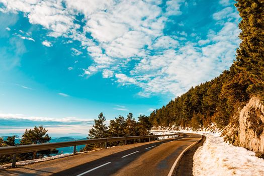 mountain road with snow in the gutter, can see the valley on the left and a thick forest on the right