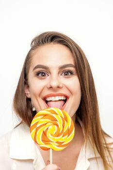 Beautiful young caucasian woman wearing a white shirt licking a lollipop on a white background