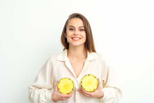 Young Caucasian smiling woman holding slices pineapple over white background, breast health concept