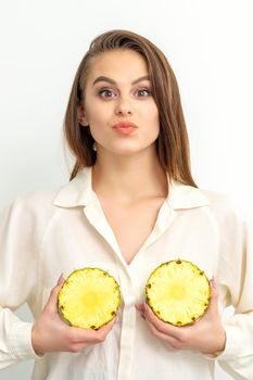 Young Caucasian smiling woman holding slices pineapple over white background, breast health concept