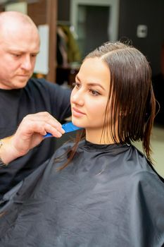 Haircut of long wet hair of young caucasian woman by a male hairdresser in a hair salon