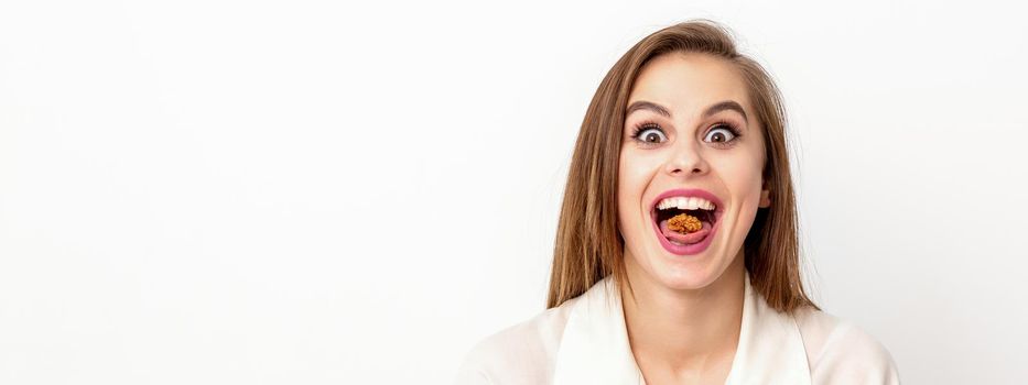 Happy young caucasian woman eating walnuts with an open mouth on white background with copy space