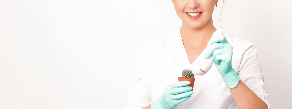 A smiling female beautician holds little green cactus with the razor in her hands. Hair removal concept