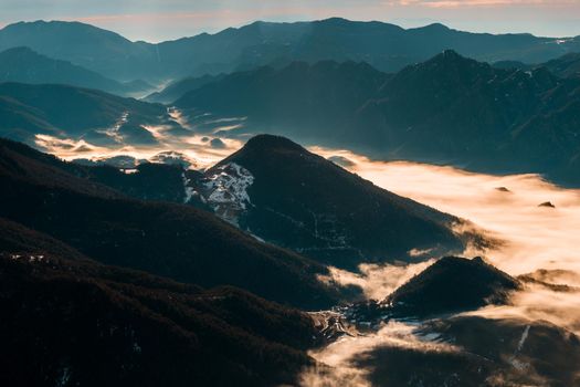 Back-lit view of a valley on a winter morning. The cold weather makes the fog stay between the mountains covering the valley like a sea of fog