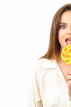 Beautiful young caucasian woman wearing a white shirt licking a lollipop on a white background