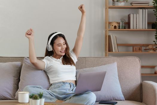 Attractive smiling young woman using laptop and listen music on sofa at home. lifestyle concept.