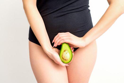 Healthy nutrition and pregnancy concept. Young woman holding one half of an avocado fruit close to her belly over a white background