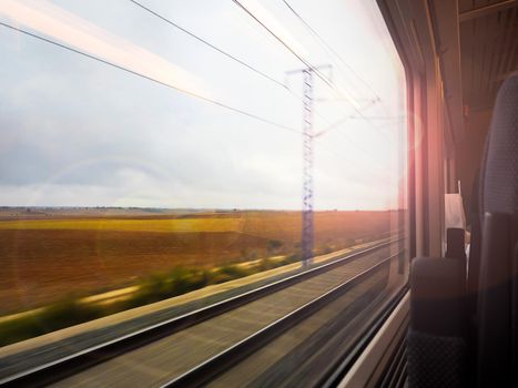 Agricultural landscape at sunset seen from the window of the moving train. Sunlight creates a soft and romantic effect. Motion blur creates a sense of speed