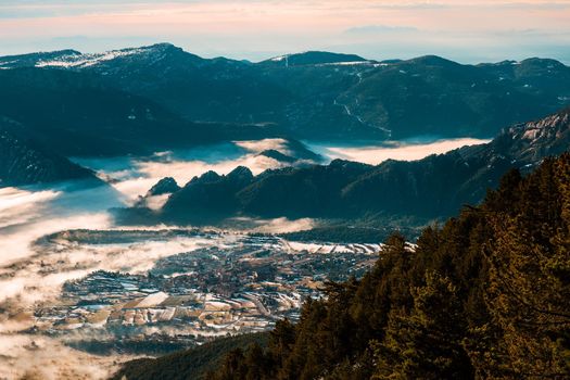 Beautiful view of a village in a valley on a winter morning, with fog covering the valley and part of the village. The cold weather makes the fog stay between the mountains like a sea of fog