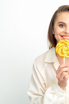 Beautiful young caucasian woman wearing a white shirt licking a lollipop on a white background