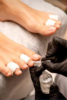 Manicure master painting nails on a female foot with transparent nail polish in a beauty salon, close up