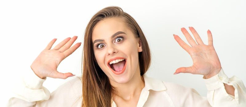 Portrait of young caucasian woman wearing white shirt raises hands and laughs positively with open mouth poses against a white background