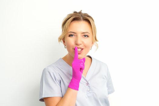 Young beautiful caucasian woman doctor, beautician doing silent gesture pressing his index finger to his lips isolated on white background