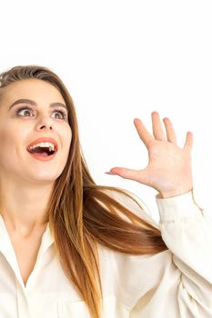 Portrait of young caucasian woman wearing white shirt raises hands and laughs positively with open mouth looking up against a white background