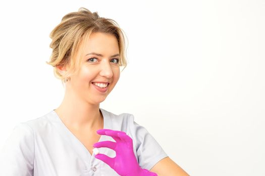 Portrait of a young smiling Caucasian beautician wearing pink gloves holding sugar cubes showing and looking at the camera against a white background