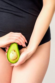 Healthy nutrition and pregnancy concept. Young woman holding one half of an avocado fruit close to her belly over a white background