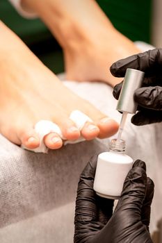 White nail polish in the hands of a manicurist while painting nails on a female feet, closeup