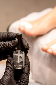 Transparent nail polish in the hands of a manicure master while painting nails on a female feet