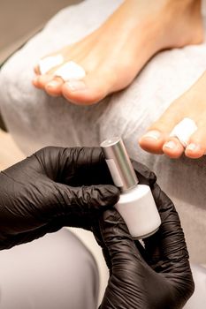 White nail polish in the hands of a manicurist while painting nails on a female feet, closeup