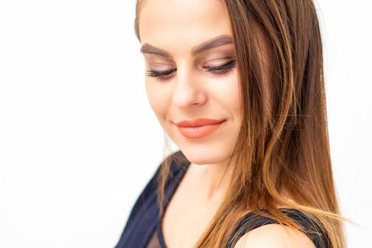 Portrait of a beautiful young caucasian smiling brunette woman with long straight hair standing and looking down on white background