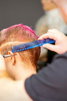 Haircut of dyed short pink wet hair of young caucasian woman by a male hairdresser in a barbershop