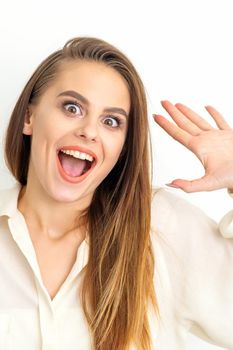 Portrait of young caucasian woman wearing white shirt raises hands and laughs positively with open mouth poses against a white background