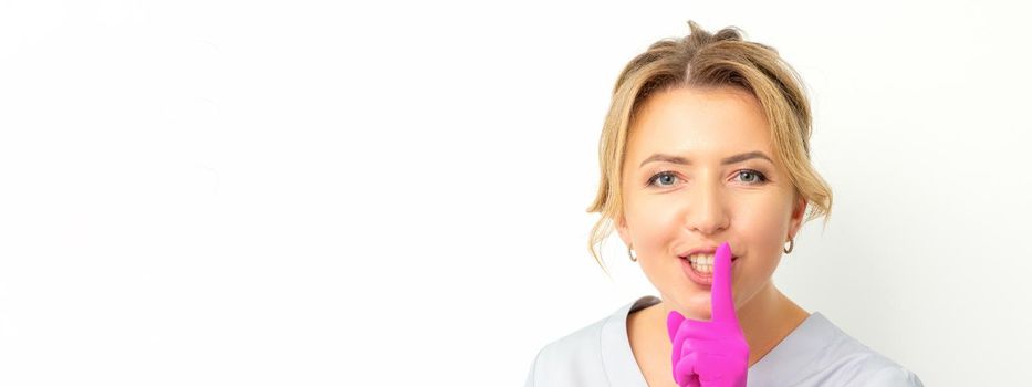 Young beautiful caucasian woman doctor, beautician doing silent gesture pressing his index finger to his lips isolated on white background