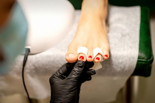 Nail painting process. A manicure master hand holds red painted fingernails on a female leg in a beauty salon