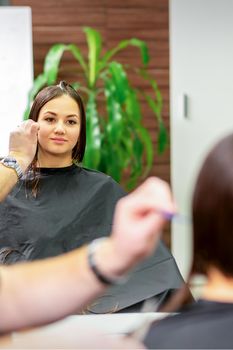 Reflection in the mirror of the young caucasian woman sitting and receiving haircut by male hairdresser at hairdresser salon